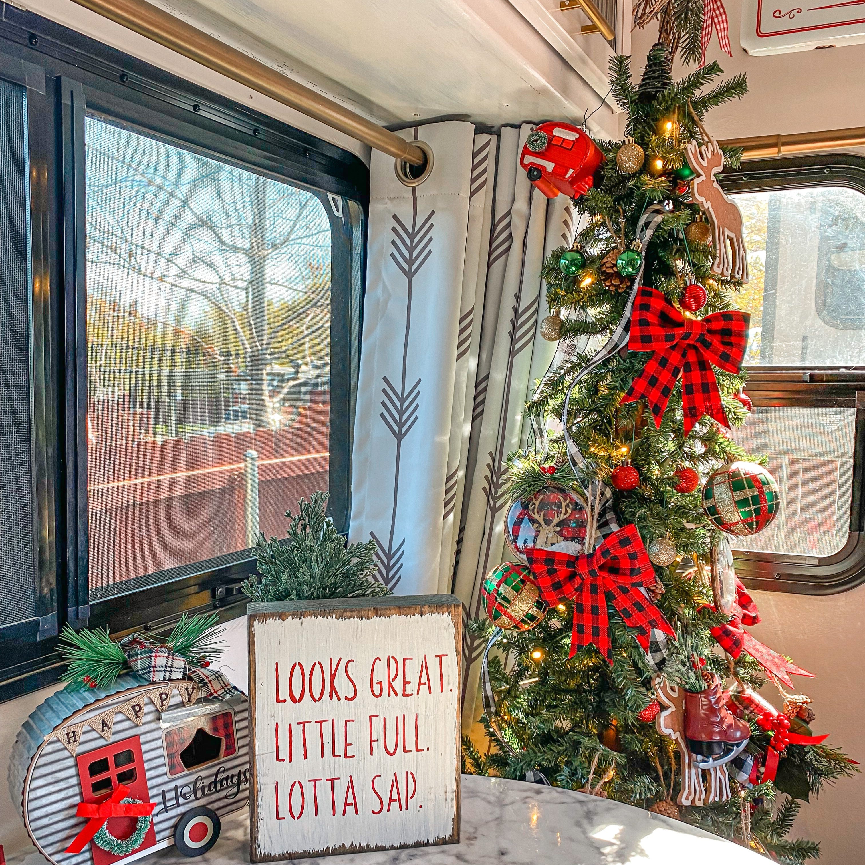 Decorated Christmas tree with red bows in a vehicle interior, featuring a sign that reads 'Looks great, little full lotta sap.'.